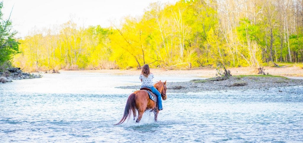 Woman crossing a river on horseback